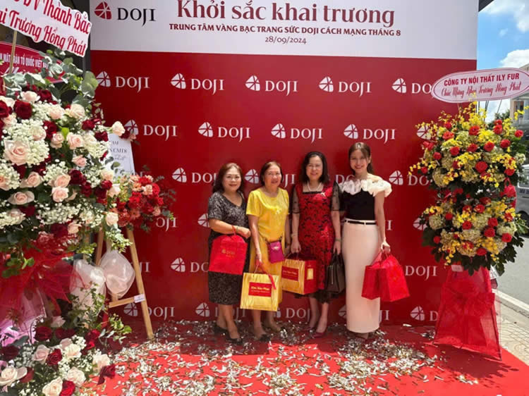 A group of women standing in front of a red wall with flowersDescription automatically generated