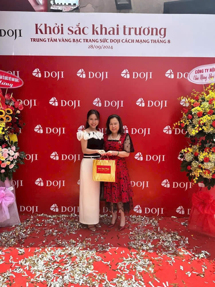 Two women standing in front of a red wall with confettiDescription automatically generated